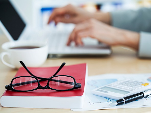 person using a laptop next to notebook and page of spreadsheets